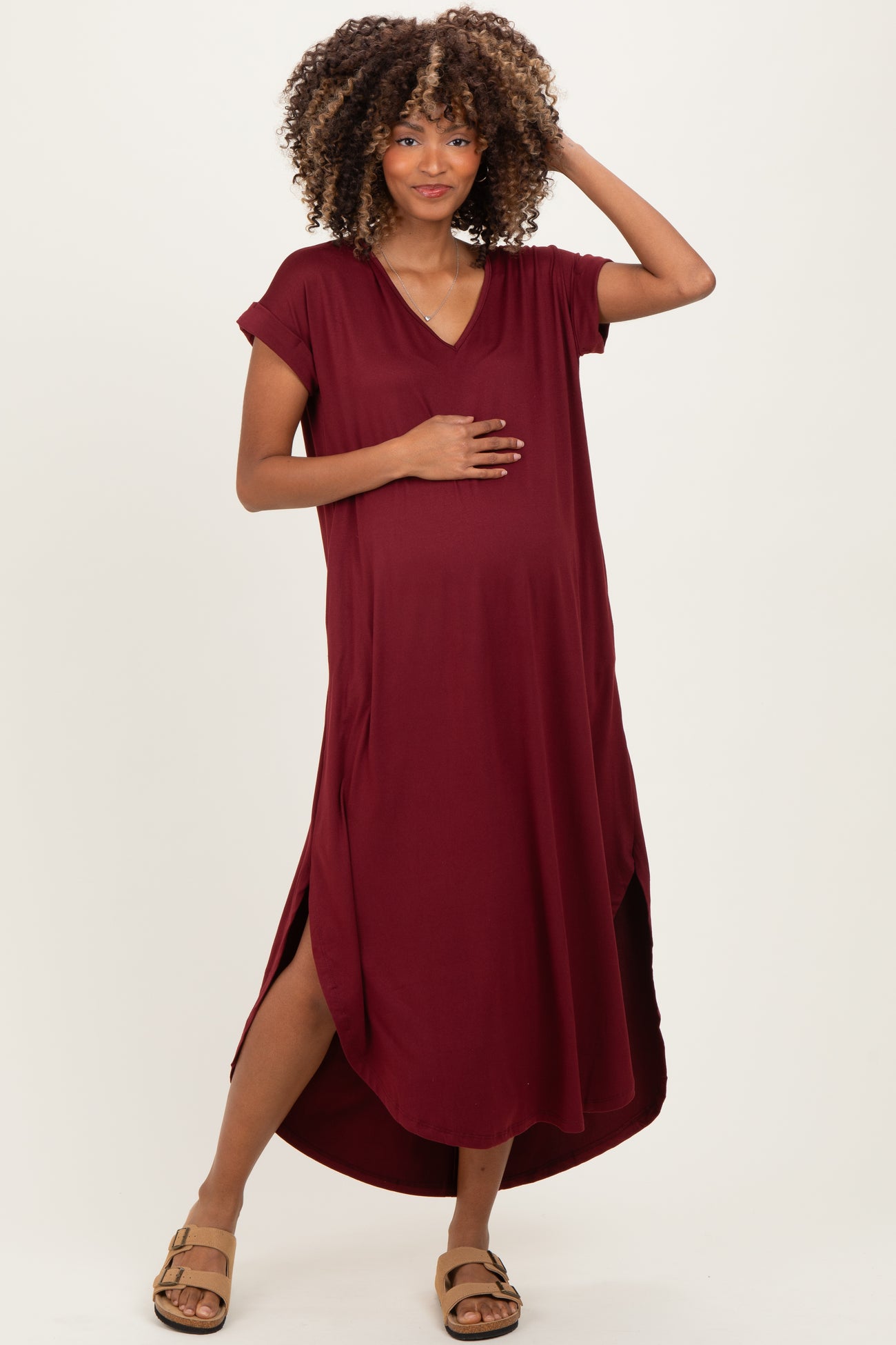 woman wearing a maroon maternity dress with short sleeves and side slits, holding her baby bump
