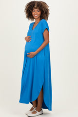 woman wearing a vibrant blue maternity dress with a side slit, gently cradling her baby bump