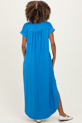 woman wearing a long blue maternity dress with short sleeves and a relaxed fit, showing a curved hem at the back