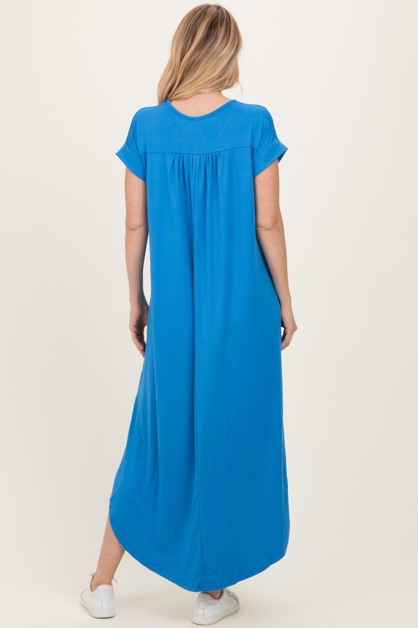woman wearing a bright blue short sleeve maxi dress with a loose fit and back pleat detail