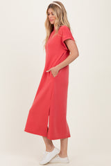 woman wearing a coral short sleeve maxi dress with side pockets and side slits, standing against a neutral background