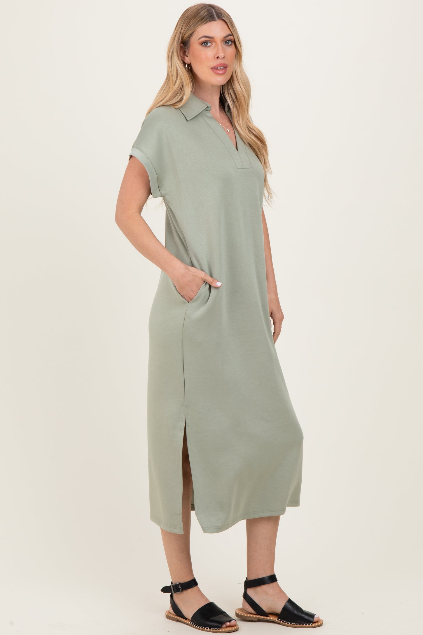 woman wearing a sage green short sleeve polo dress with side pockets and a side slit