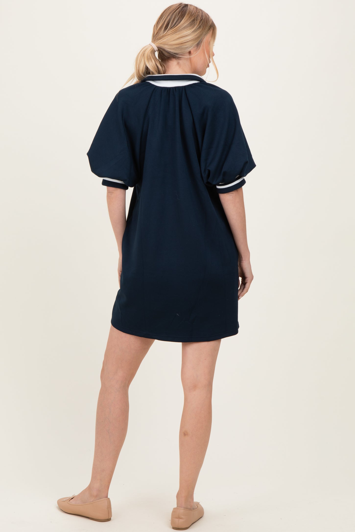 woman wearing a navy blue short sleeve dress with a white collar and puffed sleeves, shown from the back