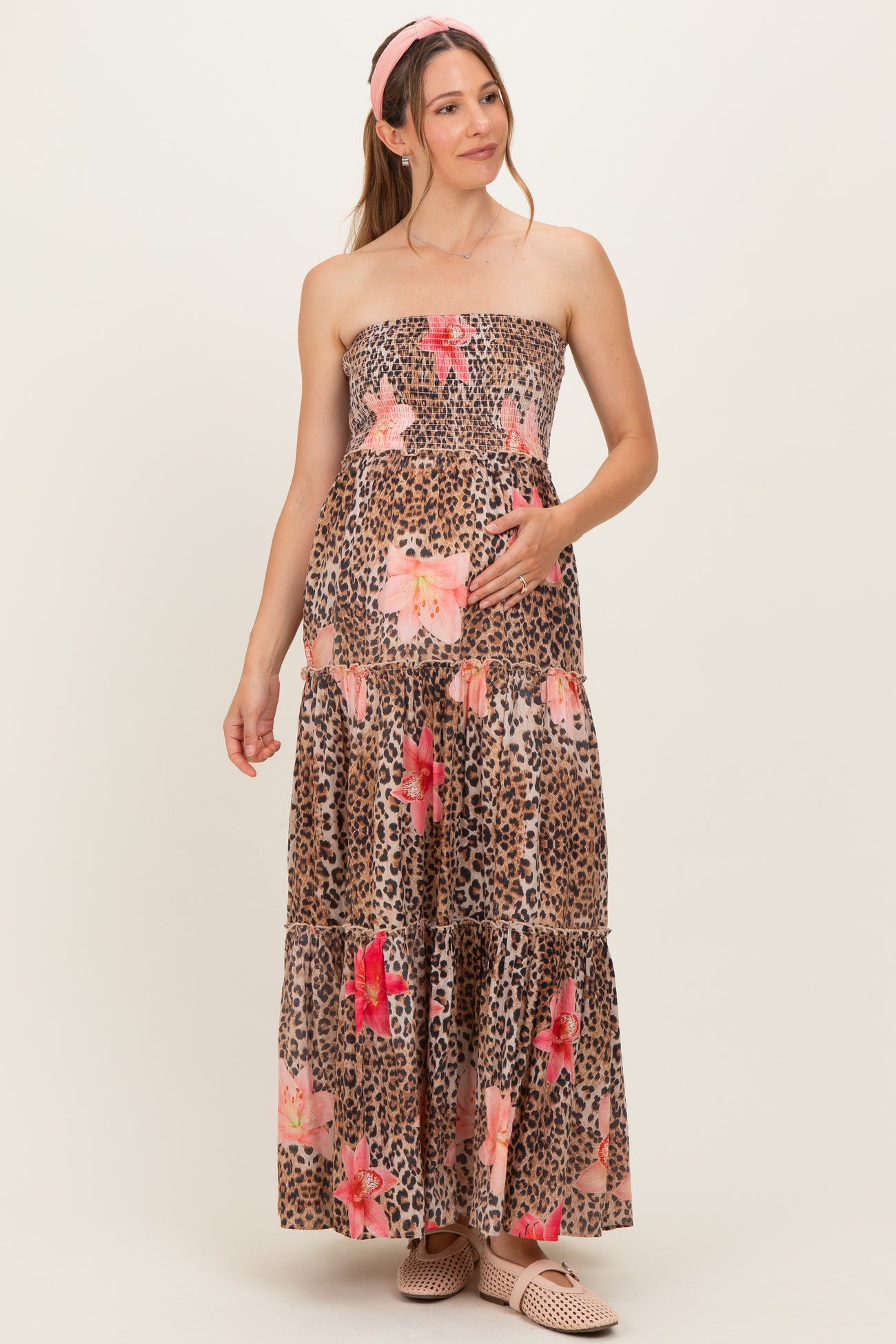 woman wearing a leopard print maternity maxi dress with floral accents and holding her baby bump