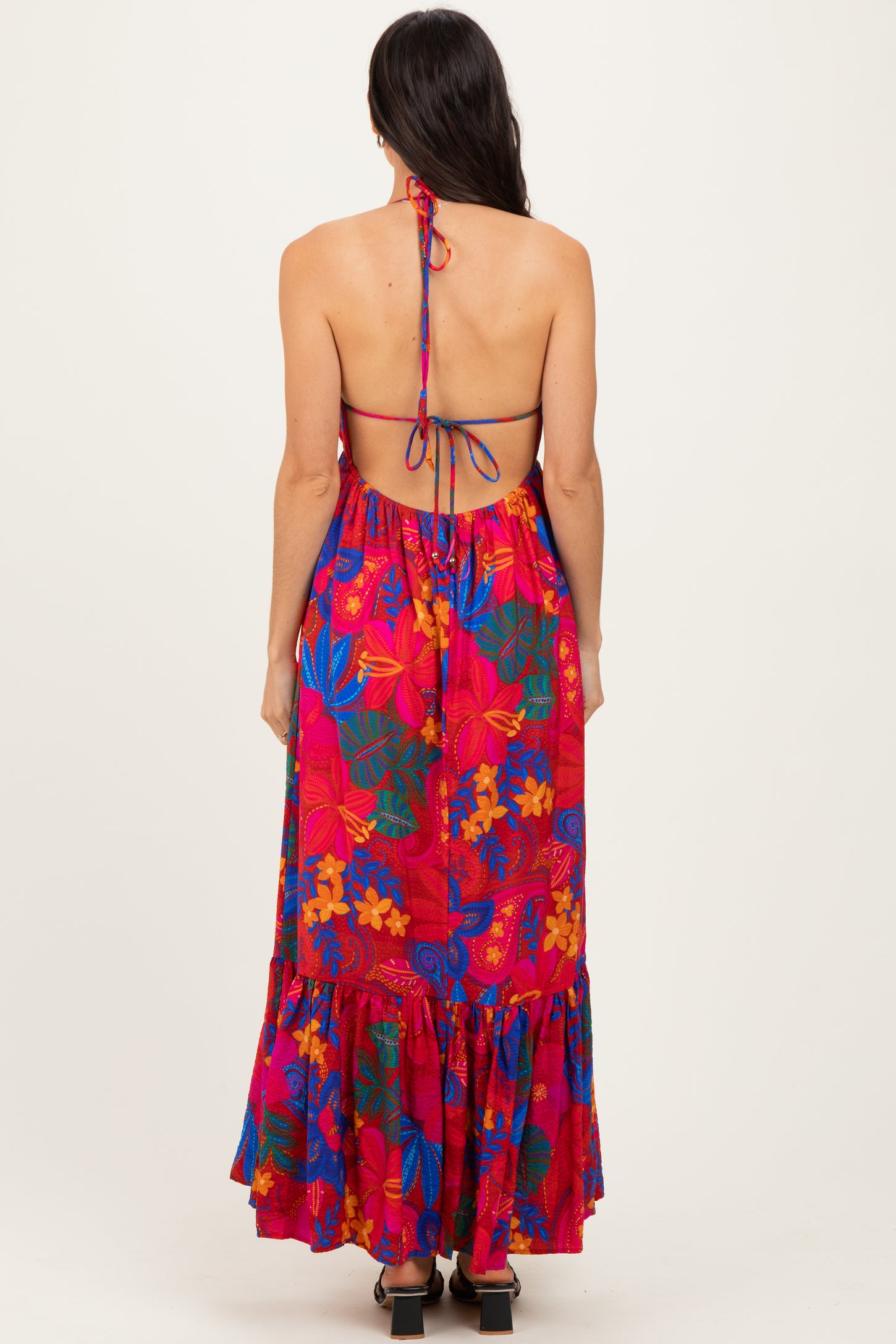 back view of a woman wearing a colorful floral maxi dress with a tie-back detail and ruffled hemline