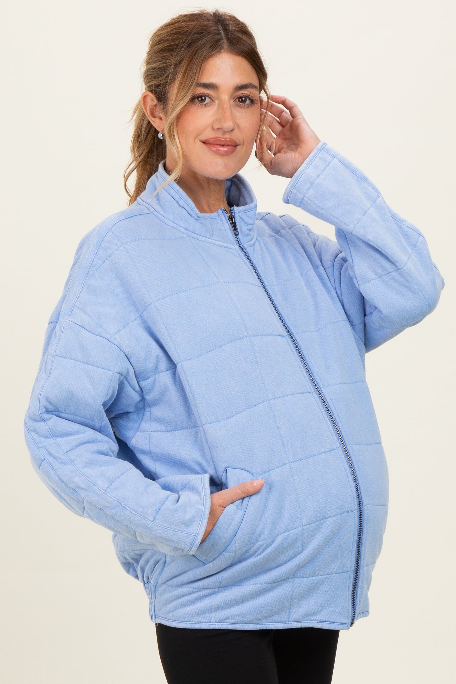 woman wearing a light blue quilted maternity jacket with a zipper and front pockets, showing her baby bump