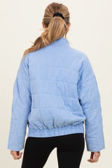 woman wearing a light blue quilted maternity jacket with a cinched waist and long sleeves, viewed from the back