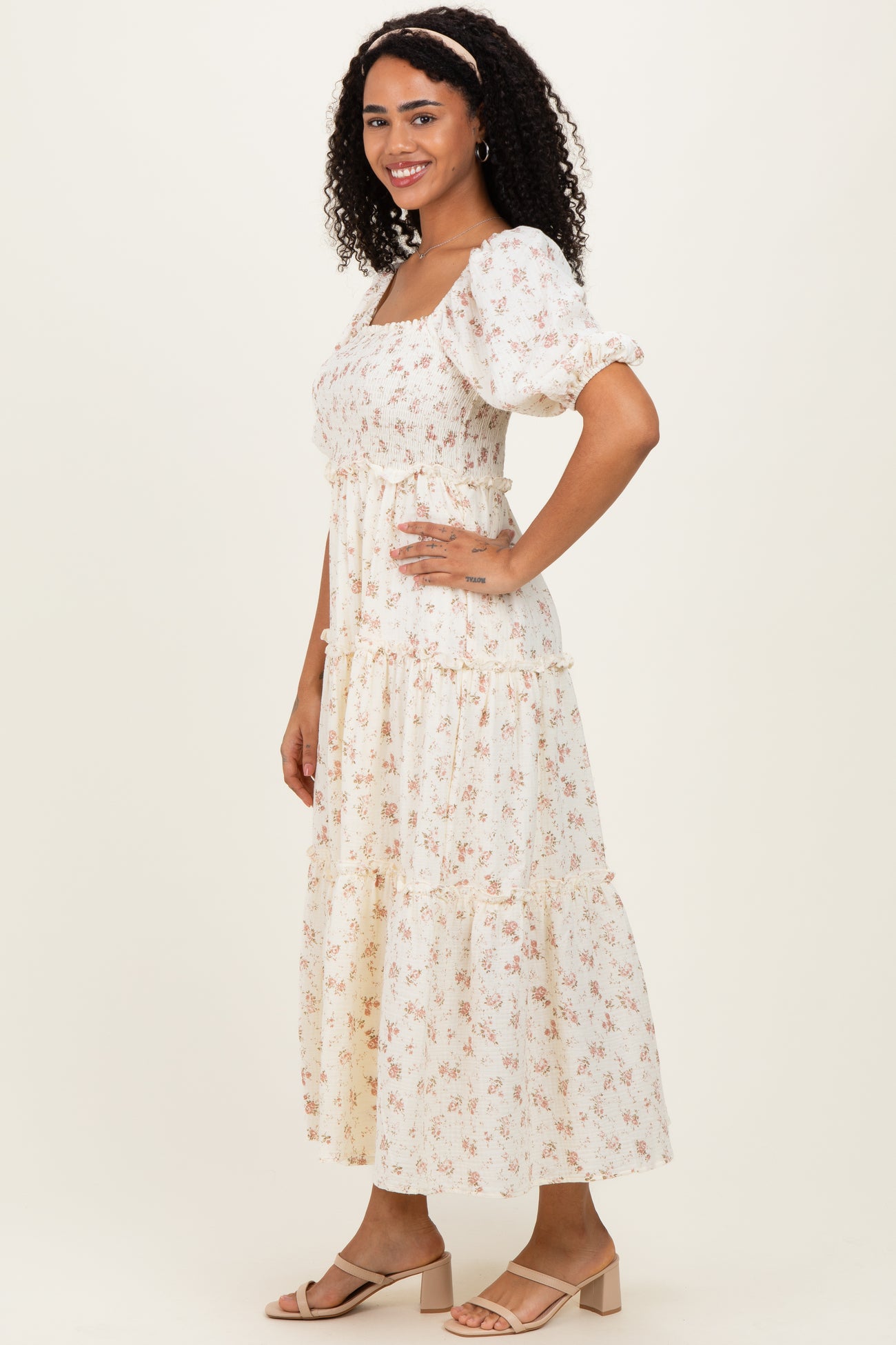 woman wearing a cream floral maxi dress with puff sleeves and tiered skirt, standing sideways against a neutral background