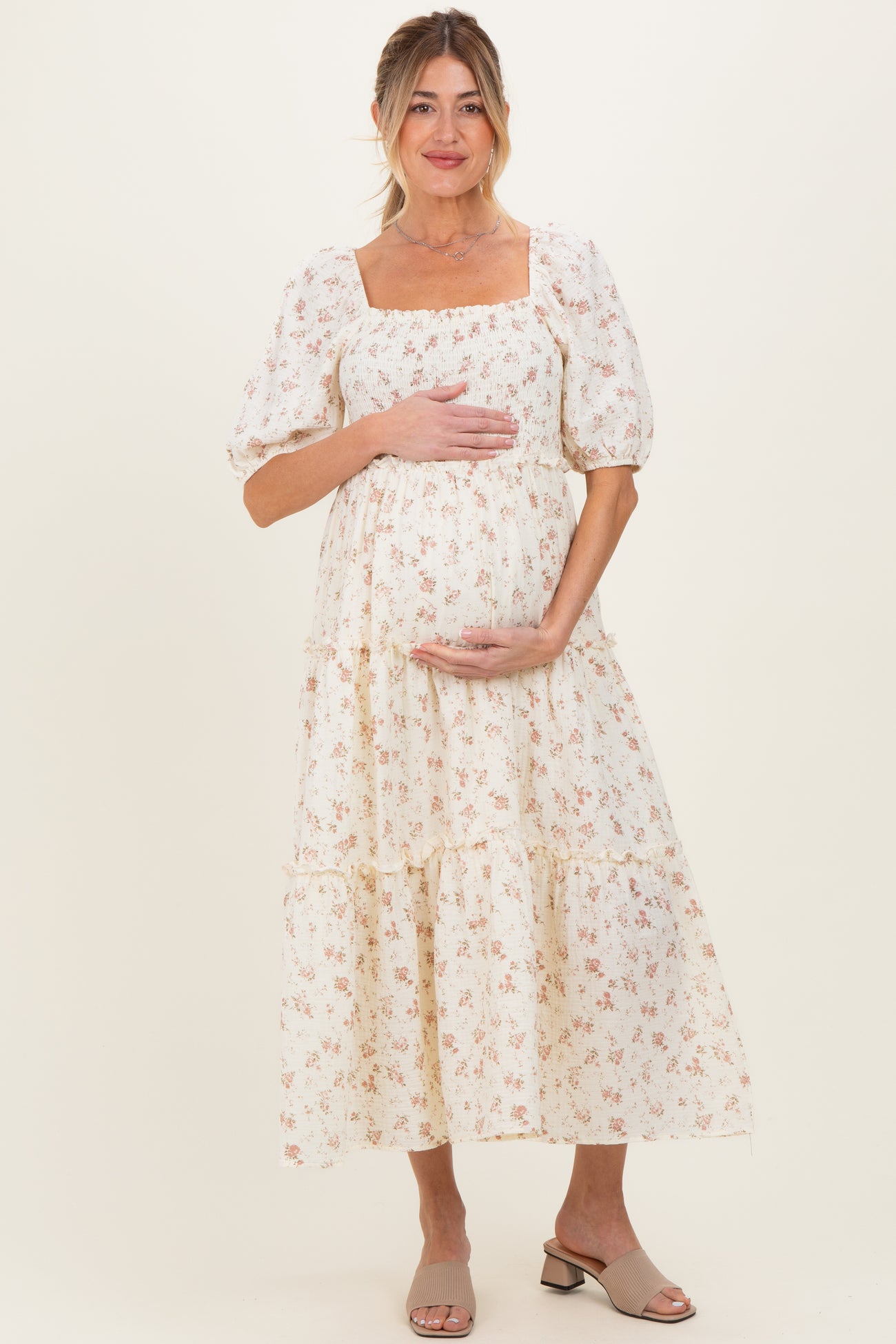 woman wearing a cream floral print maternity dress with puff sleeves and holding her baby bump