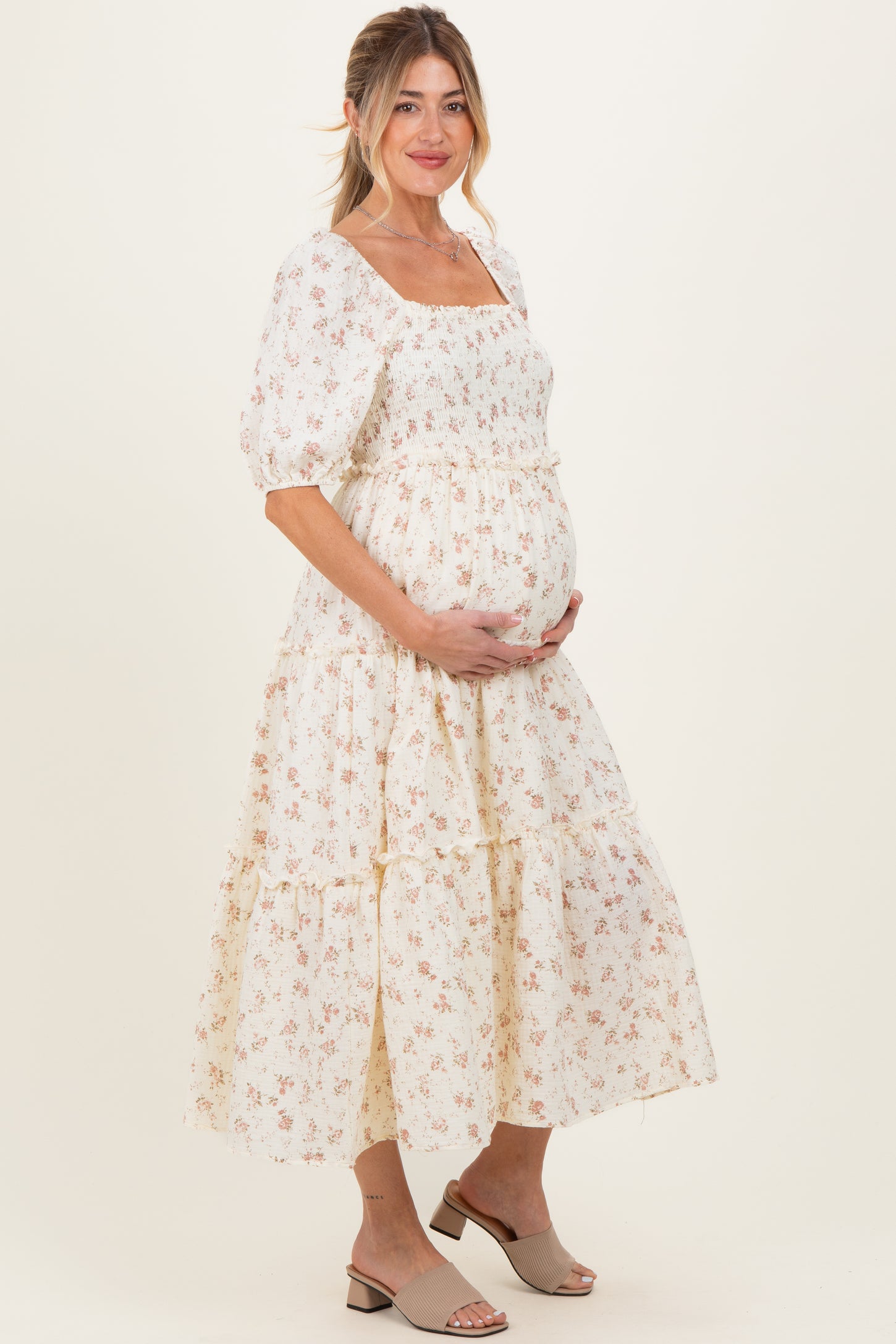 woman wearing a white floral maternity dress with puff sleeves and a tiered skirt, holding her baby bump