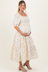 woman wearing a white floral maternity dress with puff sleeves and a tiered skirt, holding her baby bump