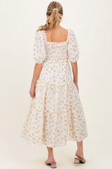 woman wearing a white floral maternity maxi dress with puff sleeves and a tiered skirt, showing her baby bump from the back