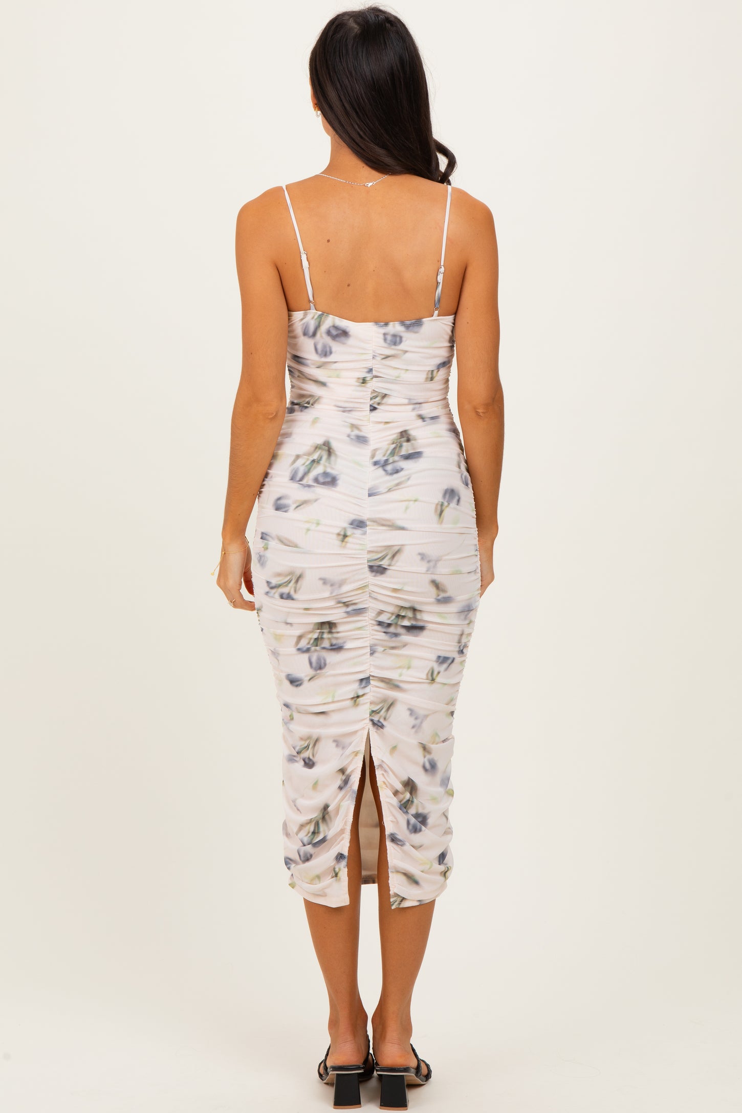 woman wearing a fitted floral midi dress with ruching and a back slit, showing the back view