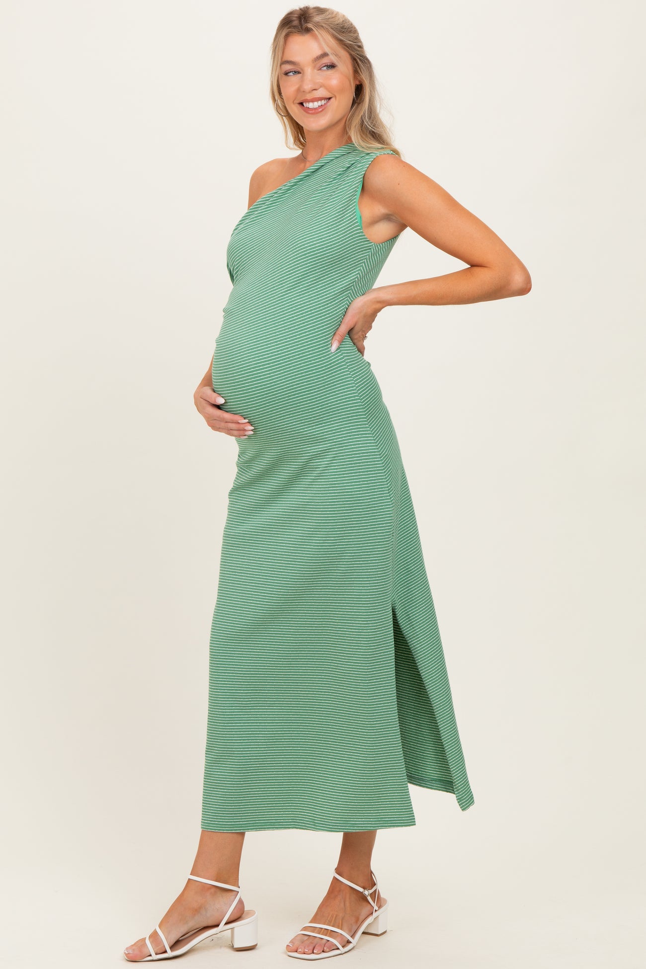 woman wearing a green one-shoulder maternity dress with a side slit and holding her baby bump