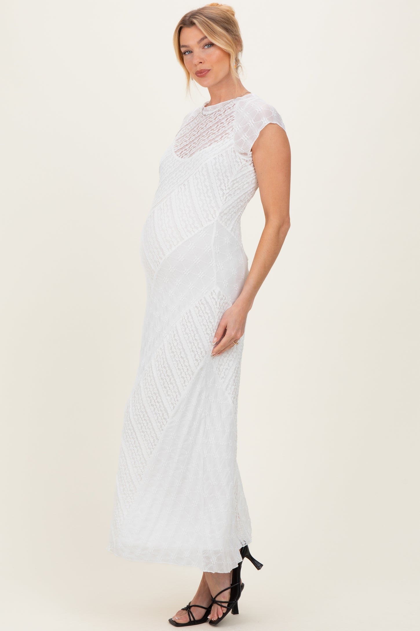 woman wearing a white lace maternity gown with cap sleeves and a fitted design, highlighting her baby bump