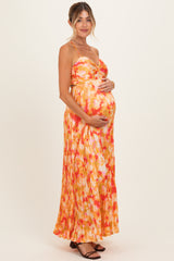 woman wearing a sleeveless orange and pink floral maternity dress, holding her baby bump