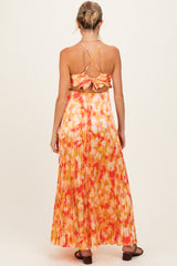 woman wearing a vibrant orange floral maternity maxi dress with a pleated skirt and crisscross back details
