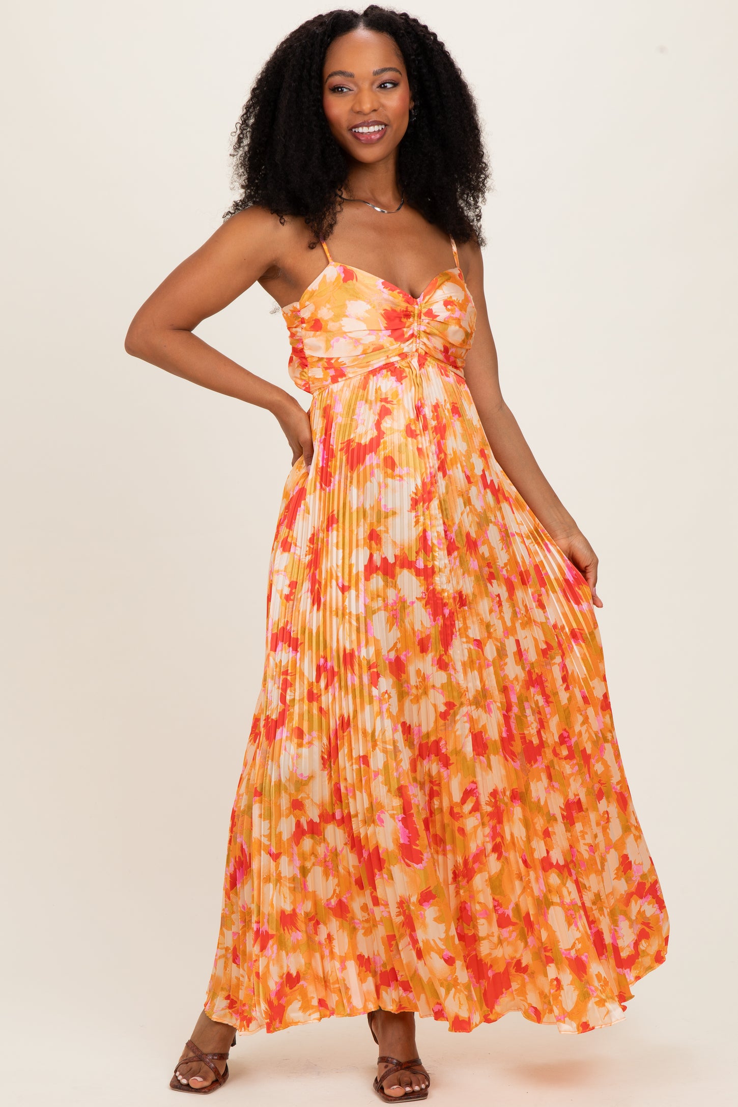 woman wearing a sleeveless pink and orange floral maxi dress with a pleated skirt and thin straps