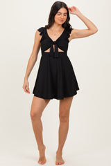 woman wearing a black ruffled swim dress with a tie-front detail and a flared skirt, standing barefoot