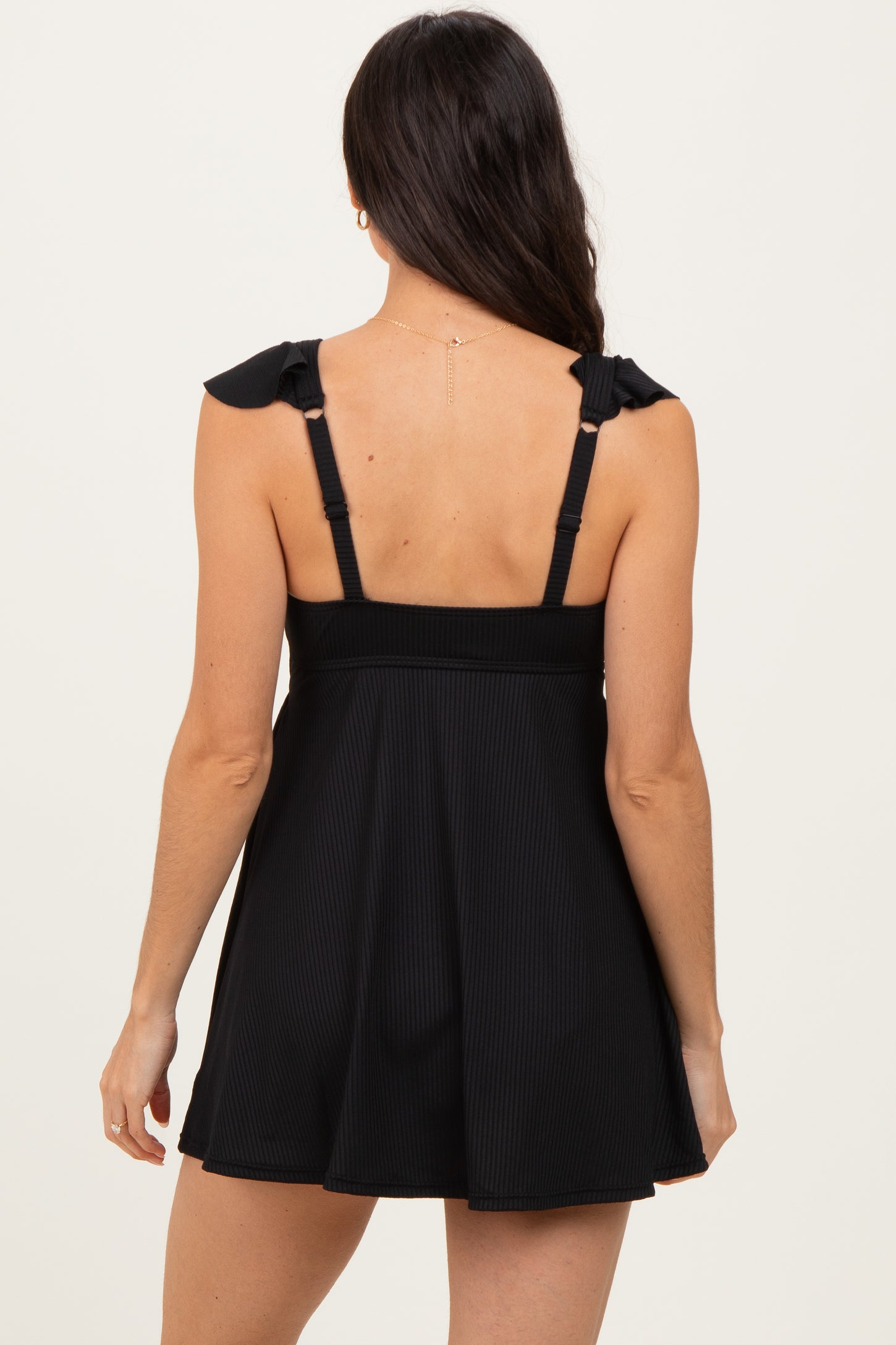 woman wearing a black ribbed swim dress with ruffled straps and flared skirt from the back