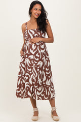 woman wearing a brown and white patterned maternity dress, holding her baby bump with a smile