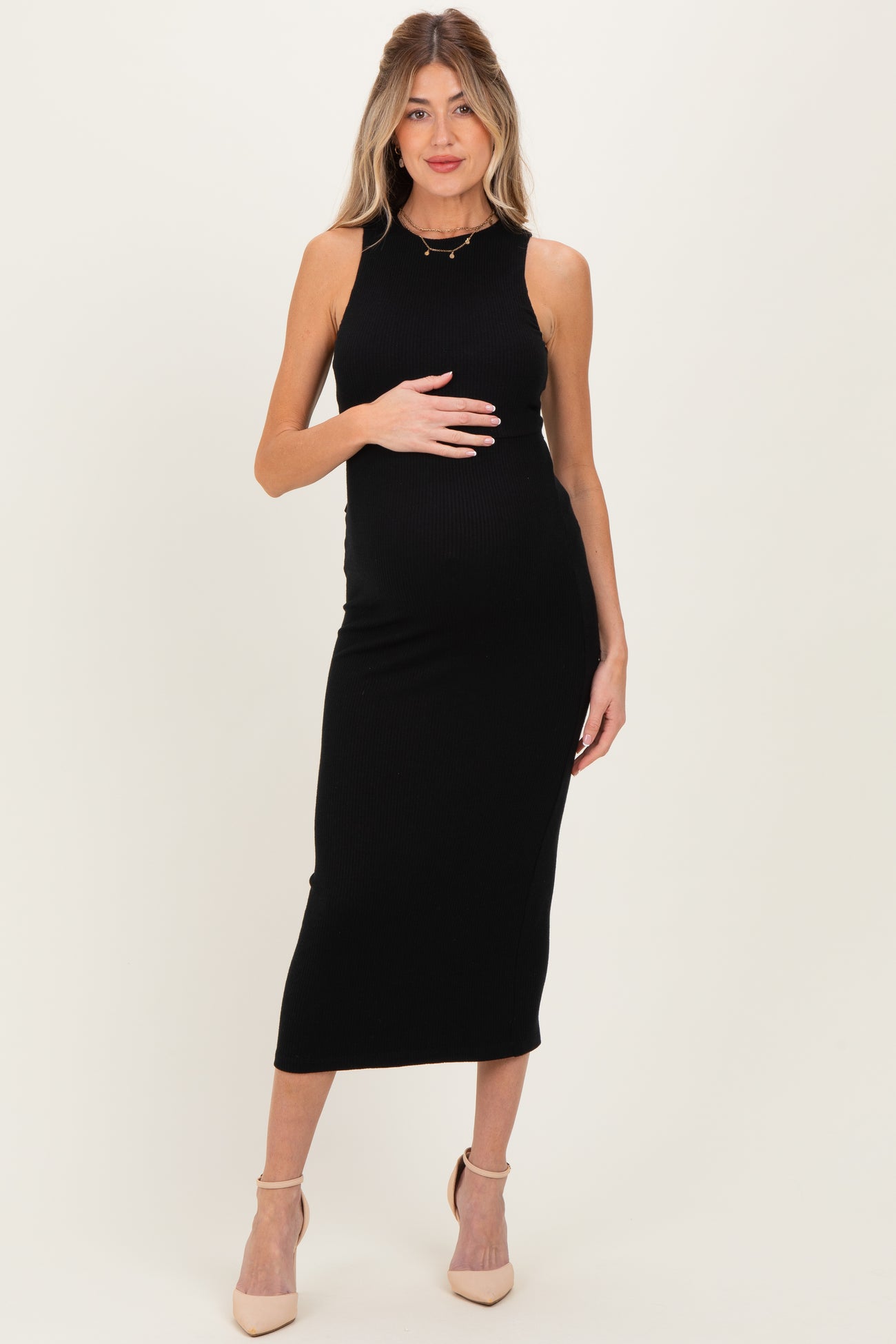 woman wearing a black ribbed maternity dress, holding her baby bump, with heels on