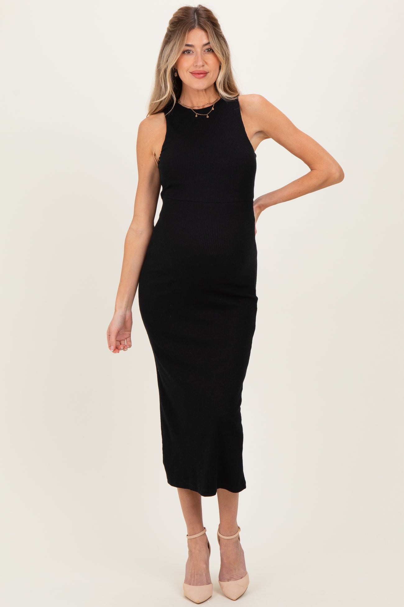 woman wearing a black ribbed midi maternity dress, posing with one hand on her hip and a visible baby bump