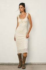 woman wearing a fitted cream-colored midi dress with ruffled straps and lace details, paired with brown cowboy boots