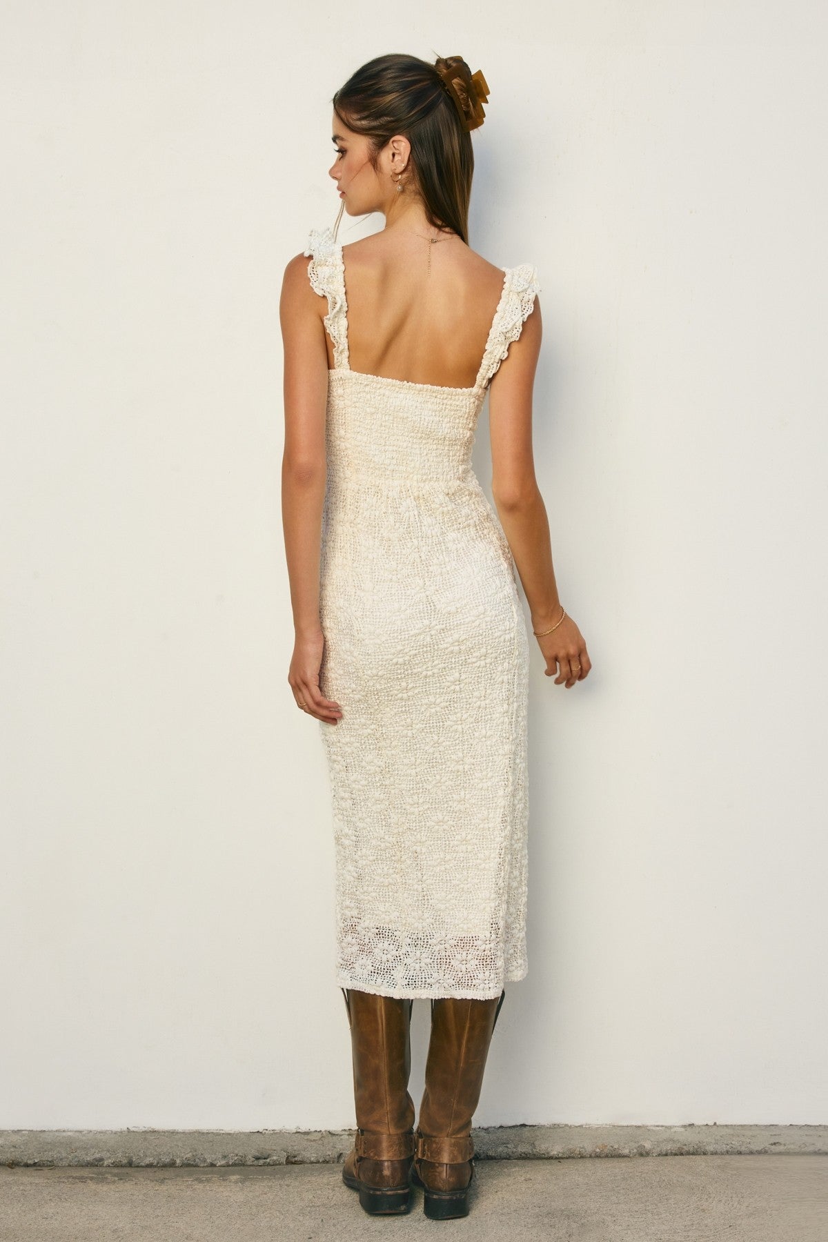 woman wearing a cream-colored lace midi dress with ruffled straps and brown knee-high boots.