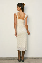 woman wearing a cream-colored lace midi dress with ruffled straps and brown knee-high boots.