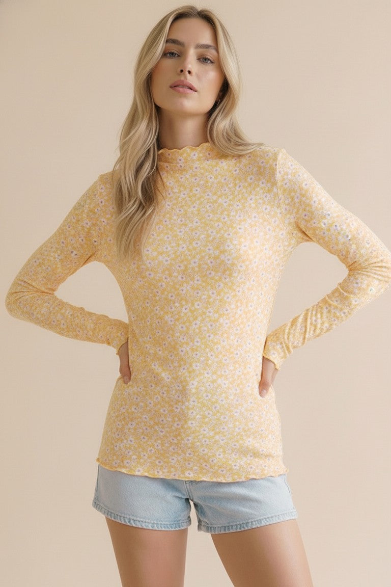 woman wearing a yellow long sleeve top with floral print and a scalloped neckline, paired with denim shorts