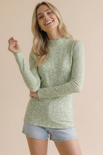 woman wearing a green long sleeve floral top with a scalloped neckline and light blue denim shorts