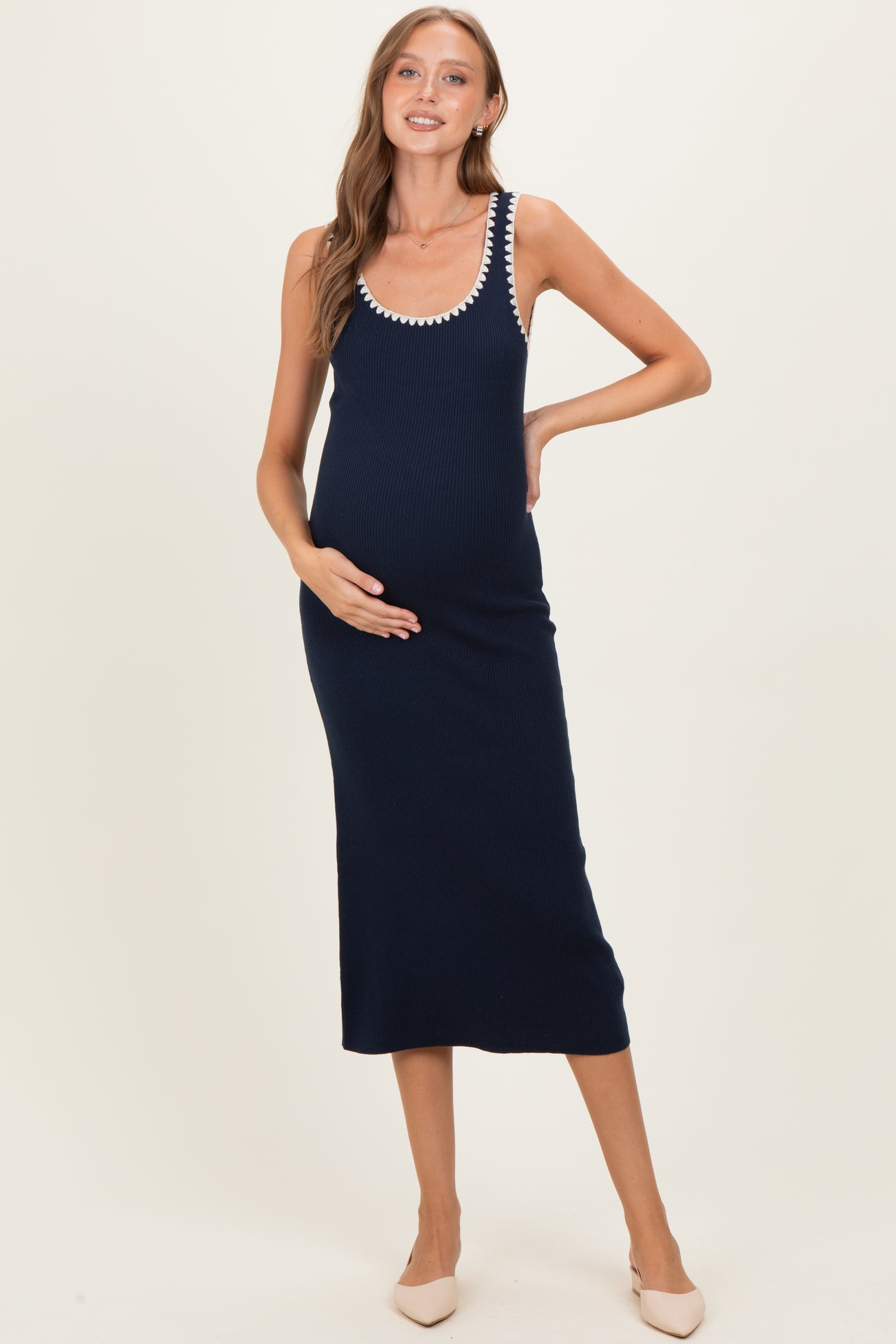 woman wearing a navy blue ribbed maternity dress with white decorative trim and holding her baby bump