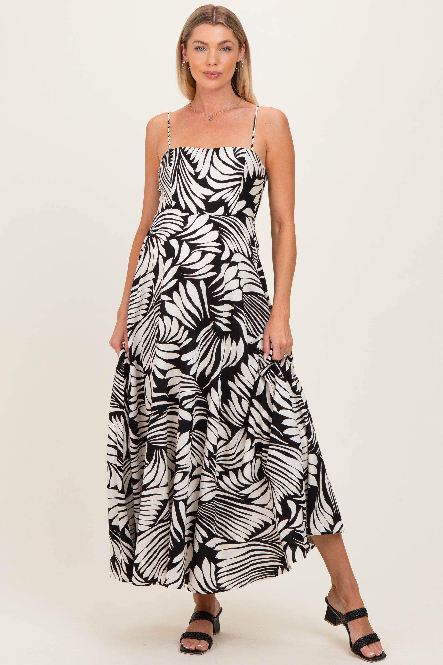 woman wearing a black and white leaf print maternity maxi dress with spaghetti straps and a flowy skirt