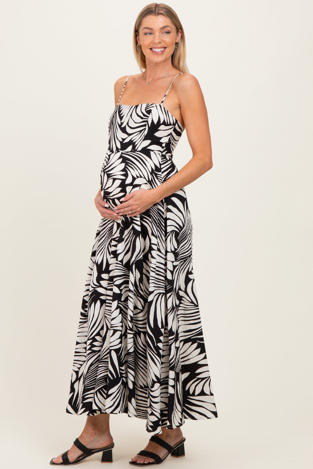 woman wearing a black and white floral print maternity dress with spaghetti straps and holding her baby bump