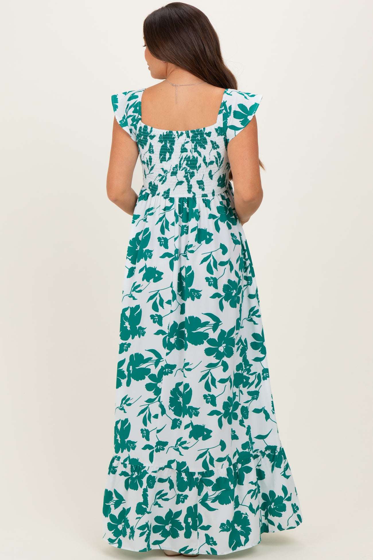 woman wearing a white maternity maxi dress with green floral pattern and smocked back, showing off her baby bump
