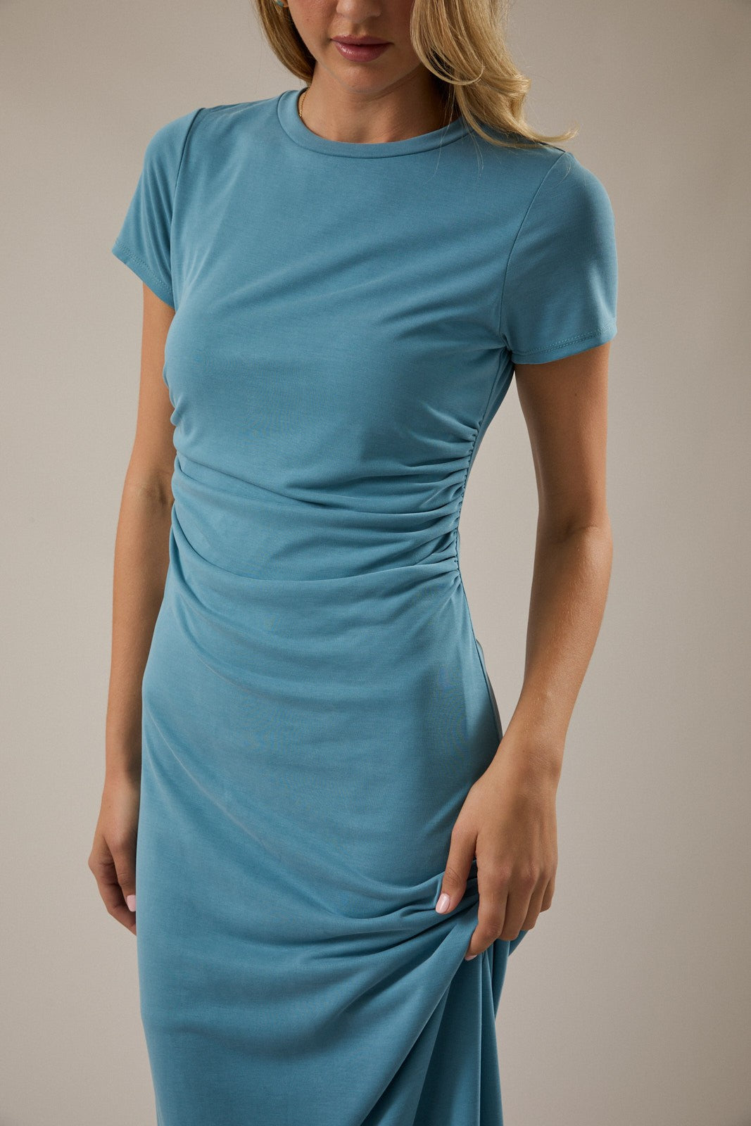 woman wearing a teal short sleeve fitted dress with ruching detail on the sides