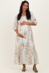 woman wearing a floral print maternity maxi dress with puff sleeves, holding her baby bump