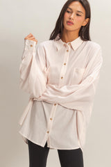 woman wearing a light pink oversized button-up shirt with a front pocket and long sleeves, styled with black leggings