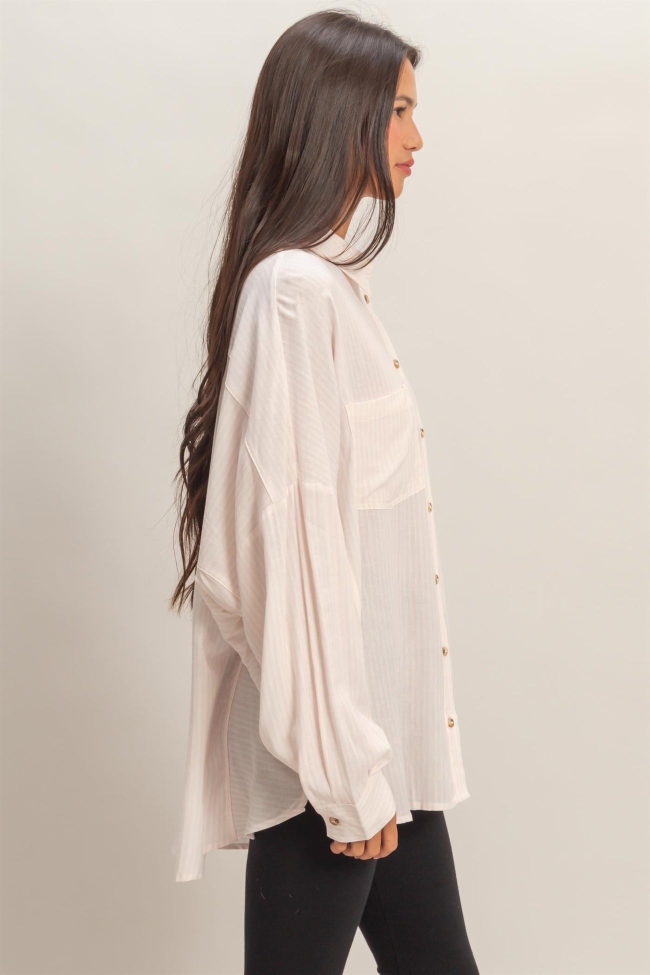 woman wearing a light pink oversized button-up shirt with long sleeves and dropped shoulders, paired with black leggings