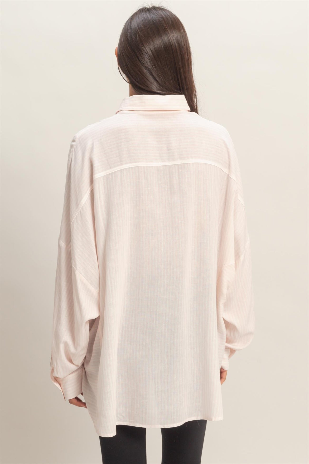 woman wearing a light pink oversized button-up shirt with long sleeves and a back yoke detail