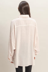 woman wearing a light pink oversized button-up shirt with long sleeves and a back yoke detail