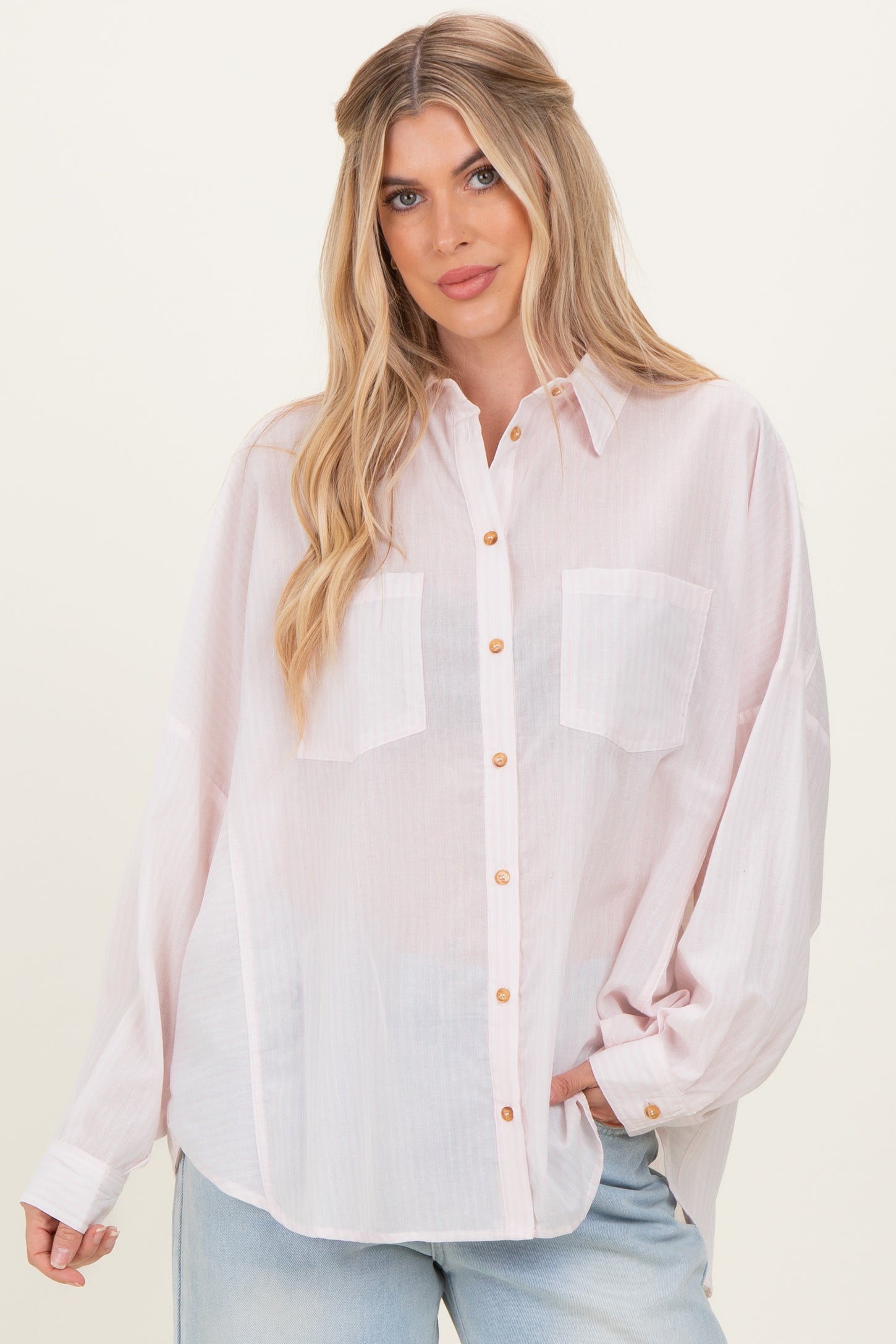 woman wearing a light pink oversized button-up shirt with two chest pockets and rolled-up sleeves