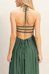 woman wearing a backless dark green maxi dress with halter neck and strappy back design