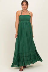 woman wearing a green halter neck maternity maxi dress with a smocked bodice and tiered ruffle hem
