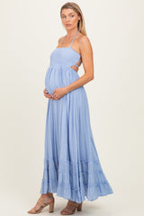 woman wearing a light blue maternity maxi dress with a smocked bodice and ruffled hem, holding her baby bump