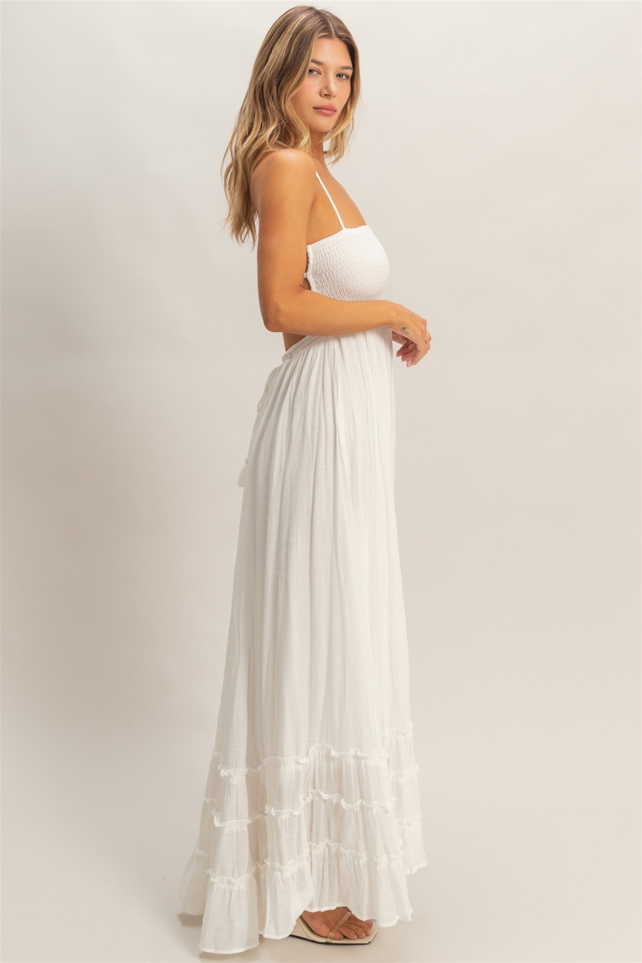 woman wearing a white maxi dress with straps, smocked bodice, and tiered ruffle hem.
