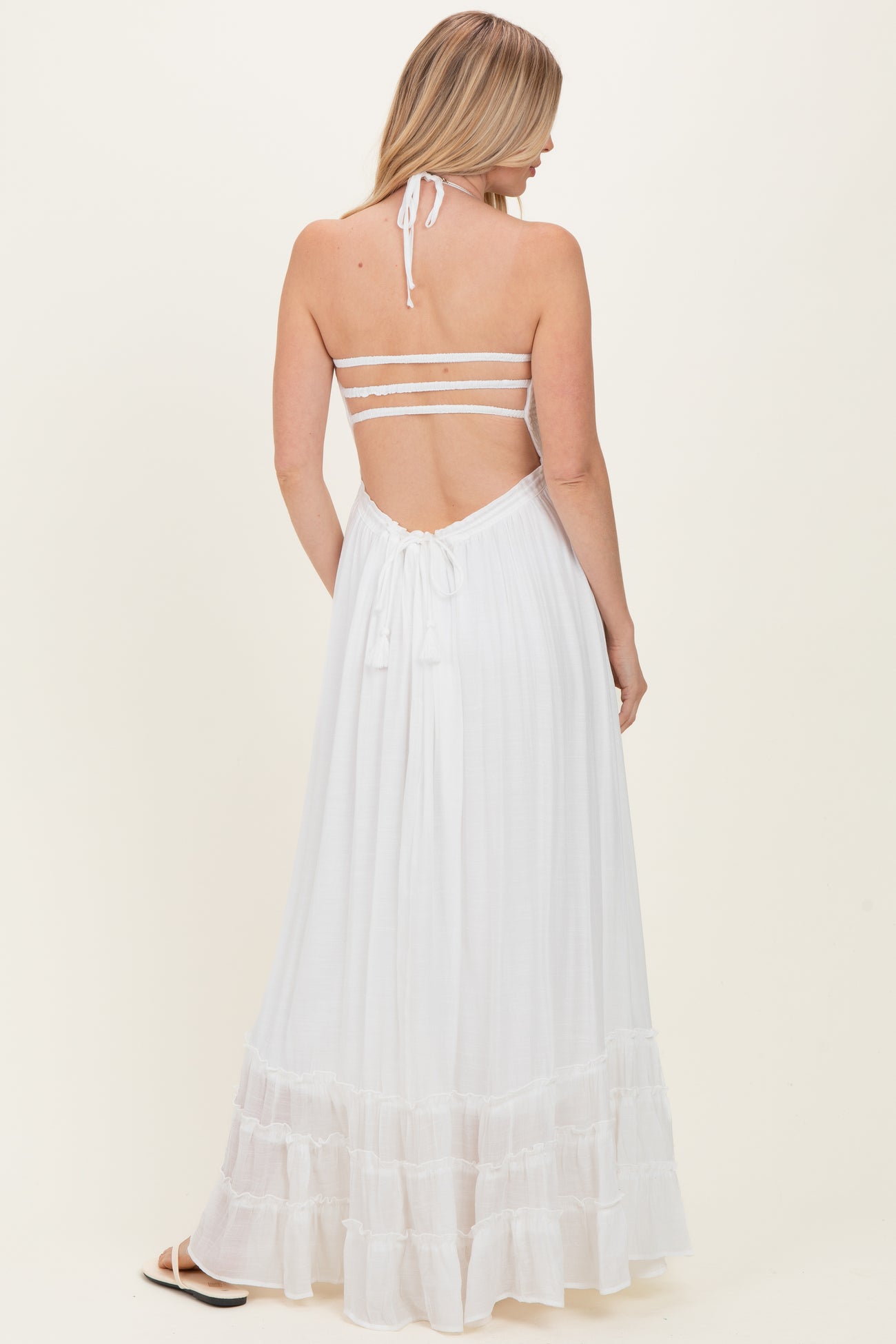 woman wearing a white halter neck maxi dress with a tiered skirt and open back detail