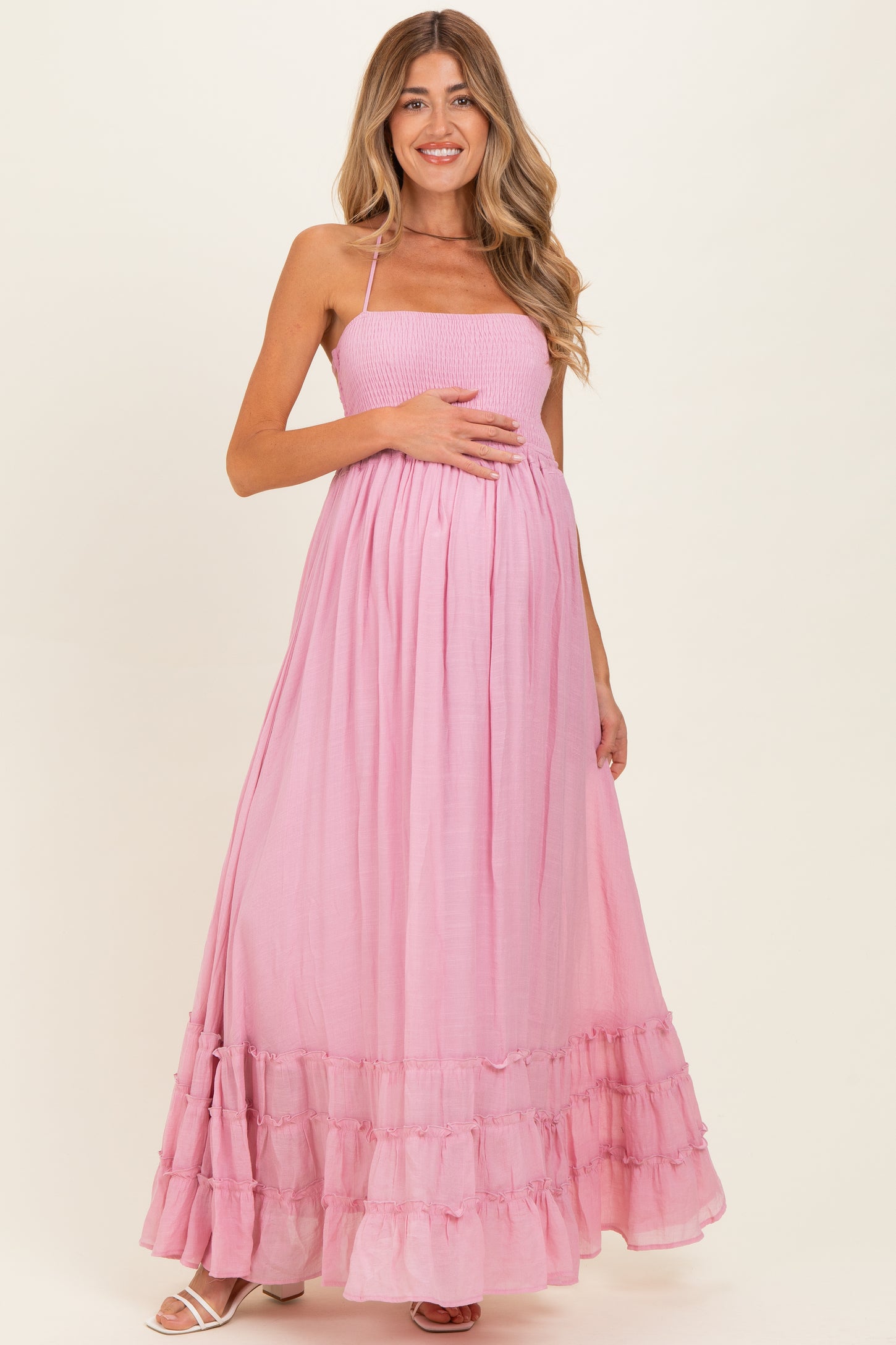 woman wearing a pink strapless maternity maxi dress with a smocked bodice and tiered ruffle hem, showing her baby bump