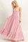 woman wearing a pink maxi dress with a smocked bodice and ruffled hem, standing and holding the skirt with both hands